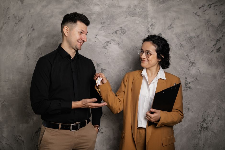 A professional solo real estate agent smiles while handing the keys to a beautiful home to a happy new homeowner, illustrating a personalized service.